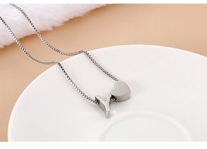 Close-up of silver heart and letter Y pendants on a fine chain in a ceramic dish