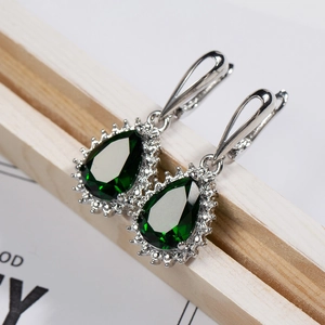 Macro view of pear-shaped emerald green zircon earrings with classic diamond halo setting