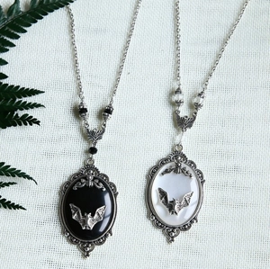 Detail of vintage bat necklaces with oval pendants and black beads on green fern leaves