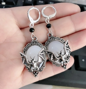 Detail of silver bat earrings featuring white oval stones and black bead accents