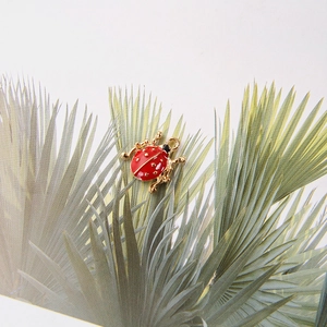 Vue macro d'un pendentif coccinelle en émail rouge avec bordure dorée sur une feuille