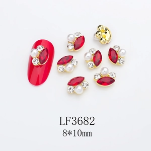 Macro detail of alloy nail charms with horse eye rhinestones and pearls on red manicure