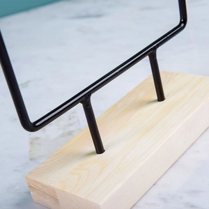 Minimalist iron earring display stand with natural wood base on white marble background