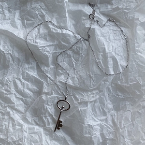 Detail shot of a silver key pendant necklace with chain on white textured paper