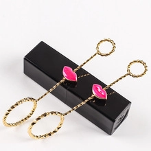 Detail showing long golden twist earrings with pink lip charm and double hoop design