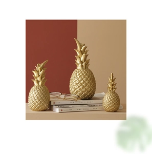 Three golden pineapple ornaments in different sizes placed on books for home decor