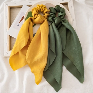 Detail view of yellow and green satin hair scrunchies with long ribbons on linen