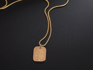 Macro detail of gold square pendant with engraved Love Alone Could Waken Love text