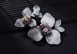 Close-up of vintage silver floral brooch with colorful stones on dark bamboo background