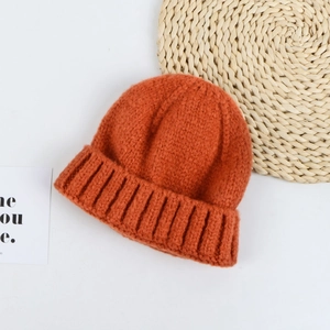 Detailed knit texture of a warm burnt orange beanie cap on a minimalist background