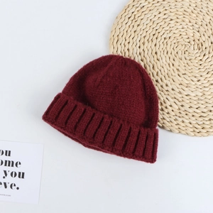 Detail of burgundy knit beanie featuring soft texture and rolled brim on rustic mat