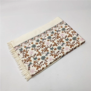 Detailed view of floral embroidery and tassels on an off-white cashmere-like shawl