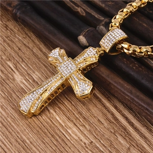 Macro shot of gold cross pendant with clear crystals on a dark wood background