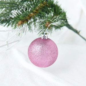 Pink glitter Christmas ball hanging on snowy pine branch for festive tree decoration