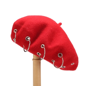Detail of red wool beret with six silver metal rings and eyelets on light wood stand