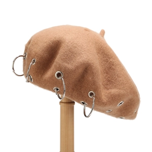 Detail of camel wool beret featuring decorative silver metal rings on a wooden stand