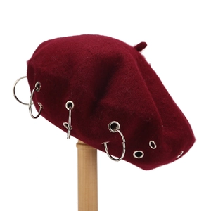 Detail of wool beret featuring silver metal rings and eyelets on a burgundy surface