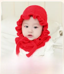 Close-up of red knitted baby bonnet with ruffled edges and secure chin ties for winter warmth