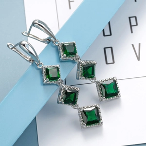 Macro shot of tiered emerald green square-cut gemstone earrings in silver setting