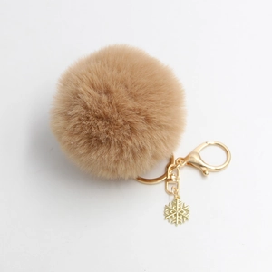 Detailopname van beige pluche pompon sleutelhanger met gouden sneeuwvlok hanger