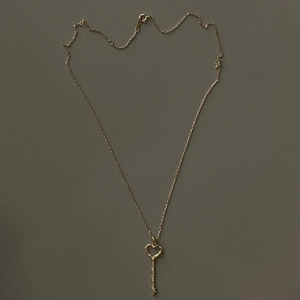 Detail view of gold heart key pendant with irregular textured stem on a delicate chain