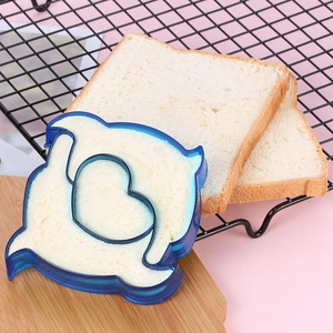 Blue dolphin-shaped plastic sandwich cutter molding a heart design on toast bread slice