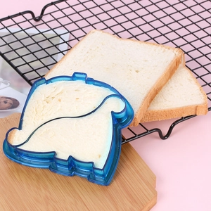Blue plastic sandwich cutter mold sealing a puppy-shaped toast on a wooden board