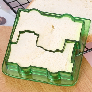Close-up of green puppy-shaped sandwich cutter slicing white toast bread on a table