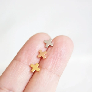 Macro shot of silver, gold, and rose gold cross stud earrings on a fingertip