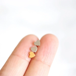 Three tiny heart stud earrings in gold and silver finish displayed on fingertips