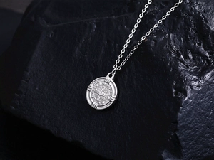 Vue macro du pendentif médaille Saint-Benoît en argent sur fond de pierre sombre