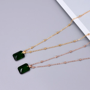 Detailed macro view of emerald green rectangular zircon pendants on satellite chains