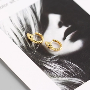 Macro shot of gold snake hoop earrings with detailed scales and black zircon eyes