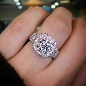 Macro shot of halo engagement ring with round white center diamond and pink side stones