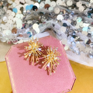 Close-up of golden starburst flower earrings with sparkling zircons on pink velvet
