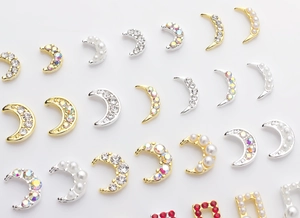 Detail of moon-shaped nail art charms with pearls and rhinestones in gold and silver