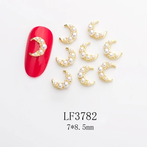 Detail of 7x8.5mm golden moon nail charms with white pearls on red manicured nail
