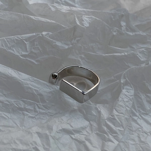 Macro shot of minimalist silver D-shaped geometric ring on textured paper background