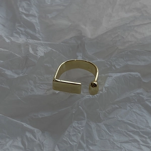 Detail view of gold geometric open ring featuring rectangular and spherical ends