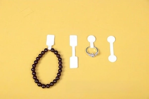 Detailed view of white adhesive jewelry price tags applied on a ring and beaded bracelet