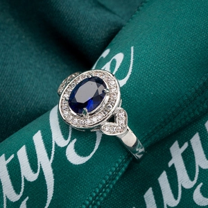 Macro shot of silver ring with oval royal blue gemstone and zircon inlay on green ribbon