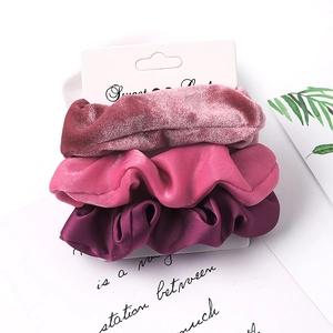Close-up of three colorful fabric scrunchies in velvet and satin on a display card