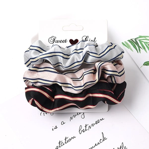 Close-up of three striped fabric scrunchies in silver, pink, and black on a white display card