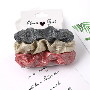 Close-up of glitter fabric scrunchies set in black gold and red on display card