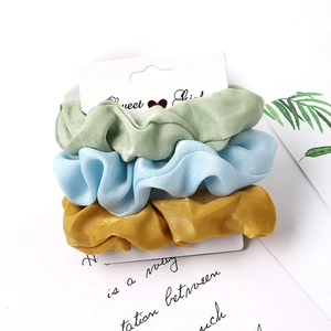 Three satin fabric scrunchies in green, blue, and gold on a Sweet Girl display card