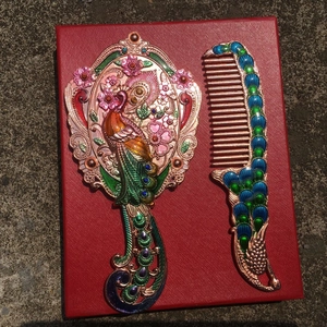 Detail of vintage peacock makeup mirror and comb set with colorful enamel inlay