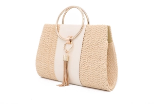 Close-up of beige woven straw handbag featuring white leather panel and gold metal tassel