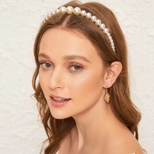 Detail of white pearl beaded headband with tulle ribbon and golden seashell earrings