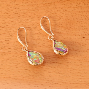 Macro detail of teardrop earrings with iridescent gemstone inlay on a wooden surface