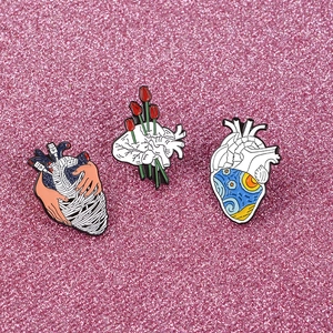 Three anatomical heart enamel pins featuring starry night and rose on pink background